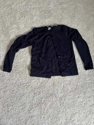 Mörk blå basic kofta med knappar - En enkel mörk blå kofta med rund hals och knäppning framtill. Långärmad modell i mjukt, tunt material som passar perfekt till lager på lager. Stilren och lättmatchad till olika outfits.