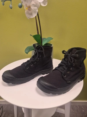 Palladium Pampa Hi Kängor Svarta EUR 43 passar 42 - Säljer ett par svarta stövletter från Palladium med högt skaft och snörning. Skorna är tillverkade i slitstark canvas med gummidetaljer på tå och sula. Klassisk rund logotyp på sidan och robust yttersula för extra grepp. Mindre i storlek som alla Palladium skor