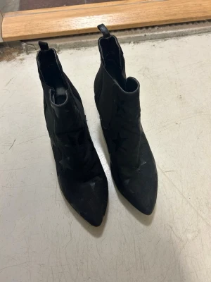 Svarta boots i mockaimitation med stjärnor  - Säljer ett par svarta boots med coola stjärndetaljer i mockaimitation. Bootsens har en elastisk resår på sidorna och låg klack vilket gör dem väldigt bekväma. Skorna kommer från Gina Tricot och är normala i storleken. 