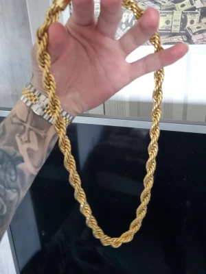 Guldfärgat tvinnat halsband - Säljer ett riktigt fett guldfärgat halsband med tvinnad design. Kedjan är grov och har en cool, snurrad form som verkligen sticker ut. Perfekt för dig som vill ha något som syns och ger en lyxig vibe. Materialet är metall med guldfinish.