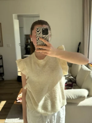 Beige volangärmad topp - Supersöt beige topp med volangdetaljer vid axlarna och rund hals. Toppen är stickad och har en mjuk, luftig känsla som passar perfekt till både jeans och kjol. Enkel men ändå unik med sina volanger som ger en extra touch. Västen är i storlek xl men sitter som en S!