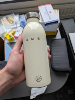 Smeg beige vattenflaska 24Bottles - Snygg beige vattenflaska från Smeg i samarbete med 24Bottles. Flaskan har en stilren design med metallock och logotyp på framsidan. Perfekt för att hålla drycken kall eller varm under dagen. Levereras med originalförpackning och skyddspåse.