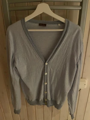 Ljusgrå kofta från Stenströms - Ljusgrå kofta från Stenströms med v-ringning och knappar framtill. Koftan har ribbade muddar vid ärmslut och nederkant samt diskret kontrastkant längs v-ringningen. Perfekt att slänga över en t-shirt för en chill look.