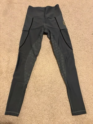 Ridtights från Maya Delorez - Snygga blå/grön/grå ridtights från Maya Delorez med hög midja och praktiska sidofickor. Materialet är stretchigt och extremt bekvämt. Fin färg dock lite slitningar i skoningen men inget som märks av egentligen. Se bild 3 och 4, därav priset. 