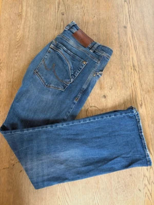 Blå jeans från LTB med raka ben - Säljer ett par klassiska blå Bootcut jeans från LTB, modell Roden. Jeansen har en knappgylf och snygga kontrastsömmar. Tillverkade i slitstark denim med fem fickor och läderpatch bak i midjan. Perfekta för en avslappnad och trendig look. Storlek W32 L32