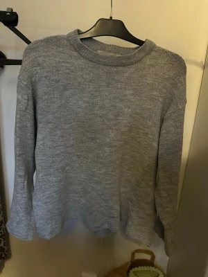 Grå stickad tröja med rund hals - En enkel och stilren grå stickad tröja med rund halsringning och långa ärmar. Tröjan har en rak passform och är tillverkad i mjukt stickat material som passar perfekt till kalla dagar.