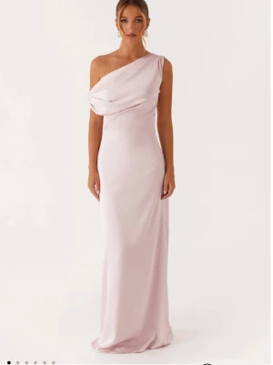 Ljusrosa oneshoulder långklänning - Elegant ljusrosa långklänning i ett mjukt, glansigt material med oneshoulder-design och draperad detalj över bysten. Klänningen har en smickrande, figurnära passform och faller snyggt längs kroppen. Perfekt för speciella tillfällen som till exempel bal eller bröllop💕