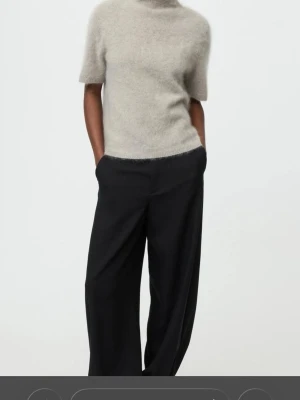 Beige stickad t-shirt från SOFT GOAT - Säljer en supermjuk och fluffig beige stickad t-shirt från SOFT GOAT. Tröjan har korta ärmar med slitsdetalh, hög krage/ turtleneck och är 100% cashmere. Perfekt för dig som gillar stilrena och trendiga plagg med en unik känsla. Helt ny!