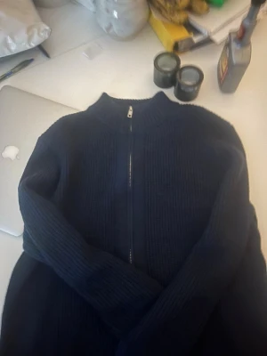 Mörkblå stickad zip-tröja - Mörkblå stickad tröja med hel dragkedja framtill och hög krage. Tröjan har ribbstickade detaljer och långa ärmar, perfekt för VÅREN🍃. Enkel och stilren design som passar till många olika outfits.