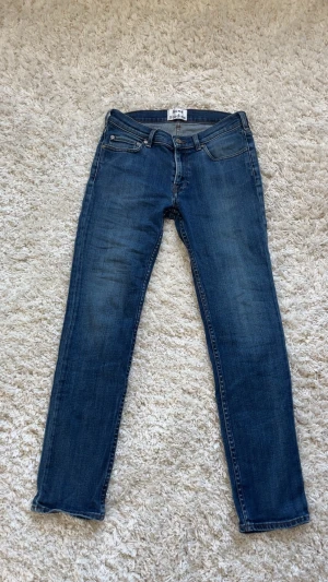 Acne Studios Jeans - Säljer ett par klassiska blå jeans från Acne Studios med rak passform och femficksdesign. Jeansen har snygga detaljer som metallknappar och är tillverkade i slitstarkt denim. Perfekt för dig som gillar stilrena och tidlösa jeans. Hör av dig om du har frågor🙌