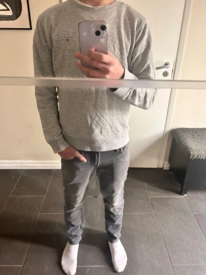 Ljusgrå sweatshirt från Gant - Jag är 165. Ljusgrå sweatshirt från Gant med rund hals och diskret logotyp broderad på bröstet. Tröjan har långa ärmar och ribbade muddar vid ärmslut och nederkant. Perfekt för en avslappnad och stilren look.