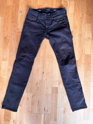 Svarta slim fit jeans från Replay - Säljer ett par svarta slim fit jeans från Nudie Jeans med klassisk femficksdesign och diskret broderi på bakfickorna. Jeansen är i storlek w31 l34.
