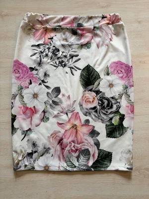 Blommig kjol med rosa och grå toner - Säljer två blommig kjolar med stora rosa, vita och grå blommor mot en ljus bakgrund och en blå. Kjolarna har rak form och elastisk midja, perfekt för dig som gillar att sticka ut med färg och mönster. Materialet känns mjukt och bekvämt. Båda ingår i priset