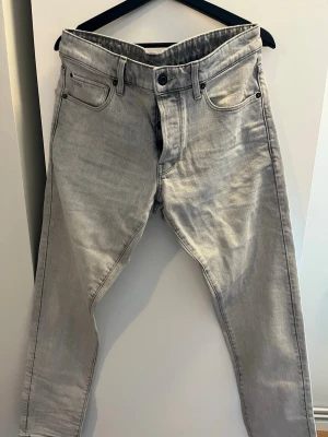G-Star RAW 3301 grå jeans - Snygga grå jeans från G-Star RAW, modell 3301 Straight Tapered. Jeansen har klassisk femficksdesign och är tillverkade i mjukt denim-material. Passformen är rak med avsmalnande ben, perfekt för en modern look. 32/34 