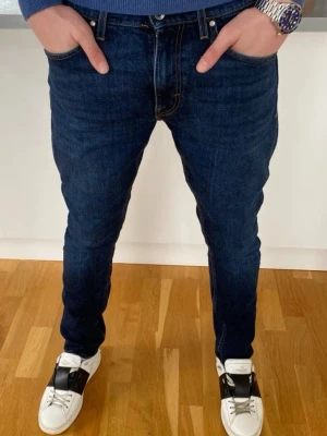 Mörkblå slim fit jeans från tiger of Sweden  - Snygga mörkblå slim fit jeans från Acne Studios med klassisk femficksmodell och läderpatch bak i midjan. Jeansen har smal passform och är tillverkade i mjuk denim med stretch för extra komfort. Perfekta för en trendig och avslappnad look.