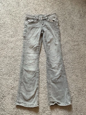 Grå bootcut jeans från Gina Tricot - Säljer ett par grå bootcut jeans från Gina Tricot. Jeansen har klassisk femficksdesign, bälteshällor och är tillverkade i denim. Perfekt för dig som gillar en avslappnad och trendig look med lite vidare ben.
