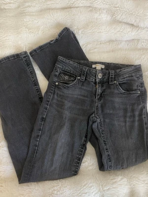 Svarta jeans - Säljer dessa svarta/mörkgrå jeansen från Gina Tricot. De är i storlek 158 och har snygg design med knappar på fickorna bak. Använda en del men inga defekter eller liknande. Midjemått:35 Innerbenslängd:74