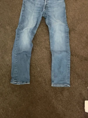 Ljusblå raka jeans - Säljer ett par ljusblå jeans med rak passform och klassisk femficksdesign. Jeansen har subtila slitningar framtill och är tillverkade i denim med en skön känsla. Perfekta till en avslappnad stil och passar till det mesta i garderoben. De har dock ett litet hål där bak som inte syns.