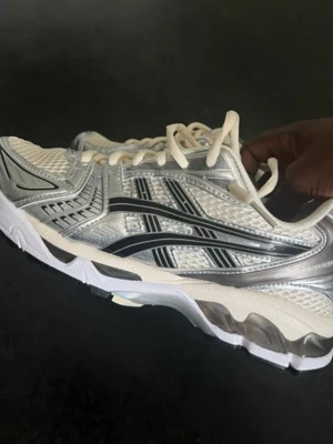 Silverfärgade Asics sneakers - Snygga sneakers från Asics i silver och vitt med svarta detaljer. Skorna har mesh- och syntetmaterial, Ortholite innersula och klassisk låg design. Perfekta för dig som gillar sportig stil och komfort.