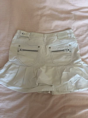 Vit skort med volang från Esprit - Snygg vit skort med volang nedtill och två bakfickor med dragkedja. Jeansmaterial och klassisk design med detaljerade sömmar. Storlek S