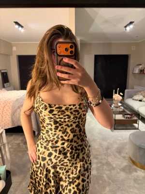 Leopardmönstrad kort klänning - Säljer en leopardmönstrad kort klänning med snörning i ryggen och smala axelband. Klänningen har en snygg och figurnära passform med öppen rygg och är tillverkad i ett glansigt material som känns lyxigt. Perfekt för dig som vill sticka ut!