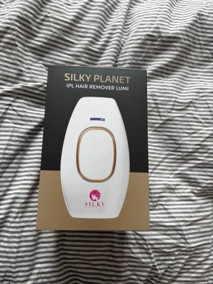 Silky Planet IPL Hair Remover Lumi - Silky Planet IPL Hair Remover Lumi är en vit hårborttagningsapparat med gulddetaljer. Den använder IPL-teknik och har 5 intensitetsnivåer för smidig och snabb hårborttagning på hela kroppen. Passar alla hud- och hårtyper och är smärtfri att använda. Det du kan se på bilderna är det som medkommer☺️