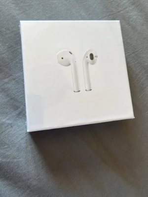 Apple AirPods med laddningsetui - Säljer ett par vita Apple AirPods med trådlöst laddningsetui. De är tillverkade i slittålig plast och har en stilren, minimalistisk design. Perfekta för dig som vill ha smidiga och snygga in-ear hörlurar med bra ljud och enkel anslutning till din iPhone.