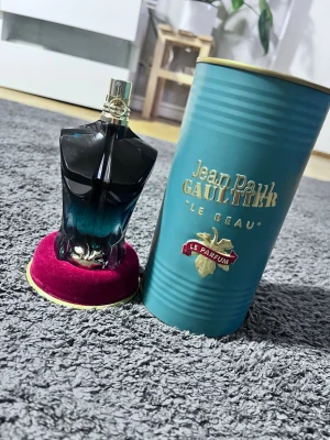 Jean Paul Gaultier parfym duo - Två parfymer från Jean Paul Gaultier: 'Le Beau Le Parfum' i en blågrön kroppformad flaska med gulddetaljer och 'Le Male Elixir' i en helguldig kroppformad flaska. Båda kommer med sina originalförpackningar och har en lyxig design.