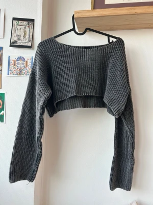 Grå cropped stickad tröja - Säljer en grå cropped stickad tröja från Urban Outfitters. Tröjan har bred ribbstickning, långa ärmar och en avslappnad passform med lite vidare halsringning. Perfekt för lager-på-lager och en chill look.