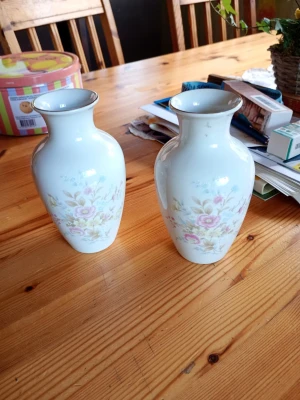 Två vita porslinsvaser med blommor - Säljer två vita porslinsvaser med mjuka former och blommigt mönster i rosa, gult och grönt. Perfekta som dekoration eller för snittblommor. Klassisk design som passar i de flesta hem.
