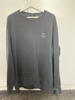 Mörkgrå sweatshirt från Neuw - Säljer en stilren mörkgrå sweatshirt från Neuw med tryck på bröstet där det står 'Stockholm Melbourne 2009'. Tröjan har rund halsringning, ribbade muddar och är tillverkad i mjuk bomull. Perfekt för en avslappnad och trendig look.
