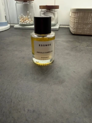ESSNCE Absolu Vanilla Eau de Parfum💛💛 - Parfymflaska från ESSNCE med doften Absolu Vanilla. Flaskan är cylindrisk i genomskinligt glas med svart lock och etikett framtill. Innehållet är gyllengult och parfymen har en söt, vaniljbaserad doftprofil. Perfekt för dig som gillar varma och mjuka dofter.
