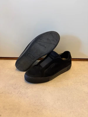 Axel Arigato – Clean 360 Laceless | Svarta minimalistiska sneakers (utgången modell) - Säljer stilrena sneakers från Axel Arigato, modellen Clean 360 Laceless (utgången). Helsvarta med minimalistisk design och elastisk slip-on för smidig passform. Tillverkade i mocka/nubuck med låg gummisula. Passar både vardag och mer dressade outfits. Använda i gott skick med normalt slitage, se bilder. Svår att få tag på då modellen inte längre tillverkas. Storlek: 41, men passar för dig som har 42,43 Pris: 949