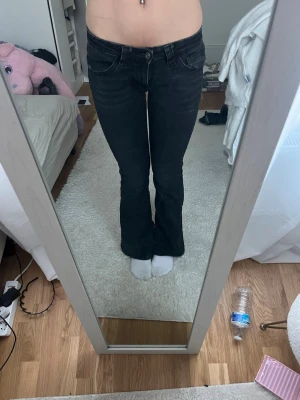 Svarta bootcut jeans med detaljer - Säljer ett par svarta bootcut jeans med låg midja och snygga sömdetaljer på bakfickorna. Jeansen har klassisk femficksdesign och är tillverkade i stretchigt denimtyg för skön passform. Perfekta för dig som gillar en trendig och avslappnad look.
