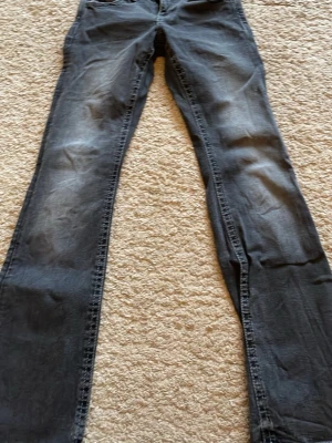 Mörkgrå jeans med detaljer bak - Säljer ett par mörkgrå jeans med utsvängda ben och snygga detaljer på bakfickorna. Jeansen har klassisk femficksmodell och kontrastsömmar. Perfekta för dig som gillar en enkel men cool stil.