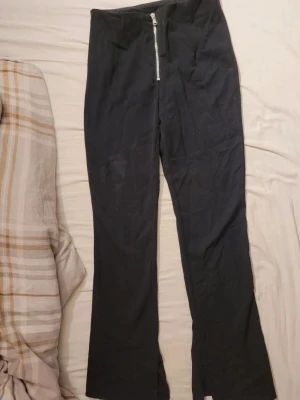 Svarta leggings med dragkedja fram - Säljer ett par svarta leggings med hög midja och silverfärgad dragkedja framtill. Modellen har raka ben och är tillverkad i ett stretchigt material som sitter bekvämt. Perfekta för en trendig och avslappnad look. Liten fläck på ena låret men går säkert bort i tvätt. 