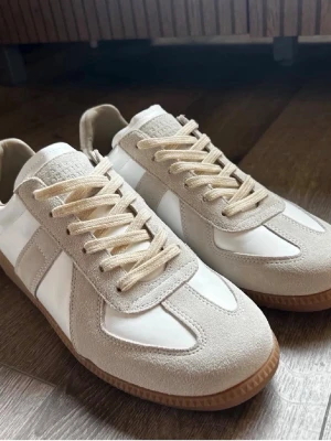 Maison Margiela Gats Vit/grå  - Riktigt fina gats ifrån Maison Margiela. Perfekt sko inför sommaren med dess snygga detaljer. Materialet är läder och mocka med en brun sula (se bilder) För små för mig tyvärr men passar dig med storlek 43-44. Box ingår självklart😀😀Vid frågor kom DM😄Pris går att diskutera