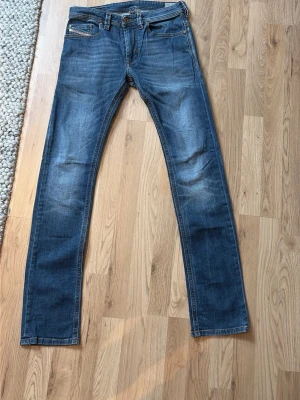 Blå raka jeans från Diesel - Modellen är 170 cm lång och väger 52 kg. Säljer ett par klassiska blå jeans från Diesel med raka ben och fem fickor. Jeansen har snygga slitningar och kontrastsömmar samt en patch med logga bak i midjan. Perfekta för en avslappnad och trendig look.