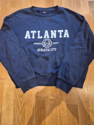 Mörkblå sweatshirt från ONLY - Cool mörkblå sweatshirt från ONLY med tryck 'ATLANTA GEORGIA STATE ATHLETIC CITY' i vitt framtill. Klassisk rund halsringning, ribbade muddar vid ärmslut och nederkant.