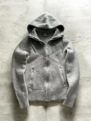 Vintage Nike kofta - Snygg grå vintage stickad hoodie från Nike med dragkedja framtill och två fickor med dragkedja. Tröjan har ribbade muddar och nederkant samt en broderad Nike-logga på bröstet. Perfekt för en chill och sportig stil. Passar som S, skick 9/10 lite luddig 