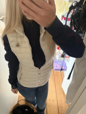 Vit pufferjacka väst från Moncler - Jättesnygg vit pufferjacka från Moncler🩷 med quiltad design och hög krage. Jackan har två fickor med dragkedja och Moncler-logga på bröstet. Perfekt nu till sommaren om man vill ha en tun jacka över sin tröja💕älskar verkligen men har redan en annan💕