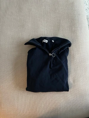 Svart halvzip-tröja från Dressman - Snygg svart långärmad tröja i storlek M från Dressman med halvzip och hög krage. Tröjan har en diskret silverfärgad dragkedja och en liten rödvit detalj på insidan av kragen.