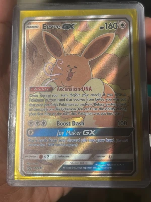 Eevee GX Pokémonkort holografiskt - Säljer ett Eevee GX Pokémonkort med holografisk yta. Kortet har 160 HP och specialförmågorna Ascension DNA, Boost Dash och Joy Maker GX. Kortet är inplastat i ett skyddsfodral och har guldkantad ram. Perfekt för samlare eller Pokémonfans.