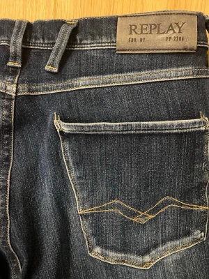Mörkblå Replay jeans limited New York med slitningar - Snygga mörkblå jeans från Replay med slitna detaljer och klassisk femficksdesign. Jeansen har kontrastsömmar, läderpatch med logga bak och smal passform. Perfekta för en trendig och avslappnad look.