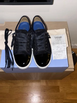 Lanvin Cap Toe  - Lanvin Sneakers – Nyskick 🔥  Säljer mina äkta Lanvin sneakers då de tyvärr inte kommer till användning. Skorna är endast använda i 2 dagar och är i sprillans nytt skick utan slitningar eller skador.  Köpta på NK för 5249 kr och kvitto finns kvar.   Kommer med originalbox, dustbag och extra skosnören.  • Storlek: US 7 / EU 43   • Skick: 10/10   • Färg: Svart/mörkblå med lackdetaljer   • Nypris: 5249 kr    Perfekta om du vill ha ett par exklusiva designer-sneakers i nästan helt nytt skick!