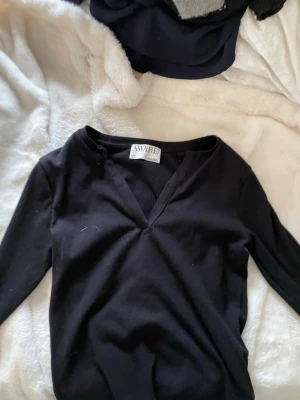 Svart ribbad topp från AWARE - Svart långärmad topp från AWARE med ribbad struktur och v-ringad hals. Enkel och stilren design som passar perfekt till jeans eller kjol. Mjuk och stretchig för en bekväm passform. Aldrig använd