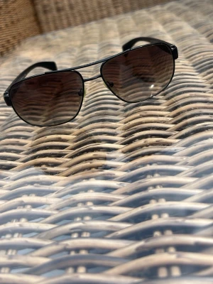 Svarta aviator solglasögon - Snygga svarta Prada solglasögon med mörka glas och tunna bågar. Samt tonat glass. Klassisk design som ger en cool vibe och passar perfekt till sommaren. Metallbågar och bekväma näskuddar för extra komfort.