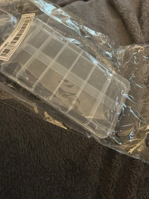 Låda av plast med lock - Praktisk låda i genomskinlig plast med lock. Formen har flera fack för att förvara och organisera. Kan användas för att sortera naglar/tippar, smycken eller andra saker