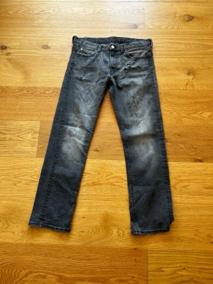 Svarta slitna jeans med raka ben - Snygga svarta jeans med raka ben och slitningar framtill. Jeansen har klassisk femficksdesign och en något tvättad look för en cool vibe. Perfekta för dig som gillar en avslappnad och trendig stil. Vet inte storlek då de inte står på jeansen men skulle gissa på W32 L32 då dom är lite baggy! 