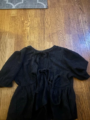 Svart blus med knytning Gina Tricot - Svart blus från Gina Tricot med snygg struktur i tyget och flera knytband framtill. Blusen har korta ärmar.